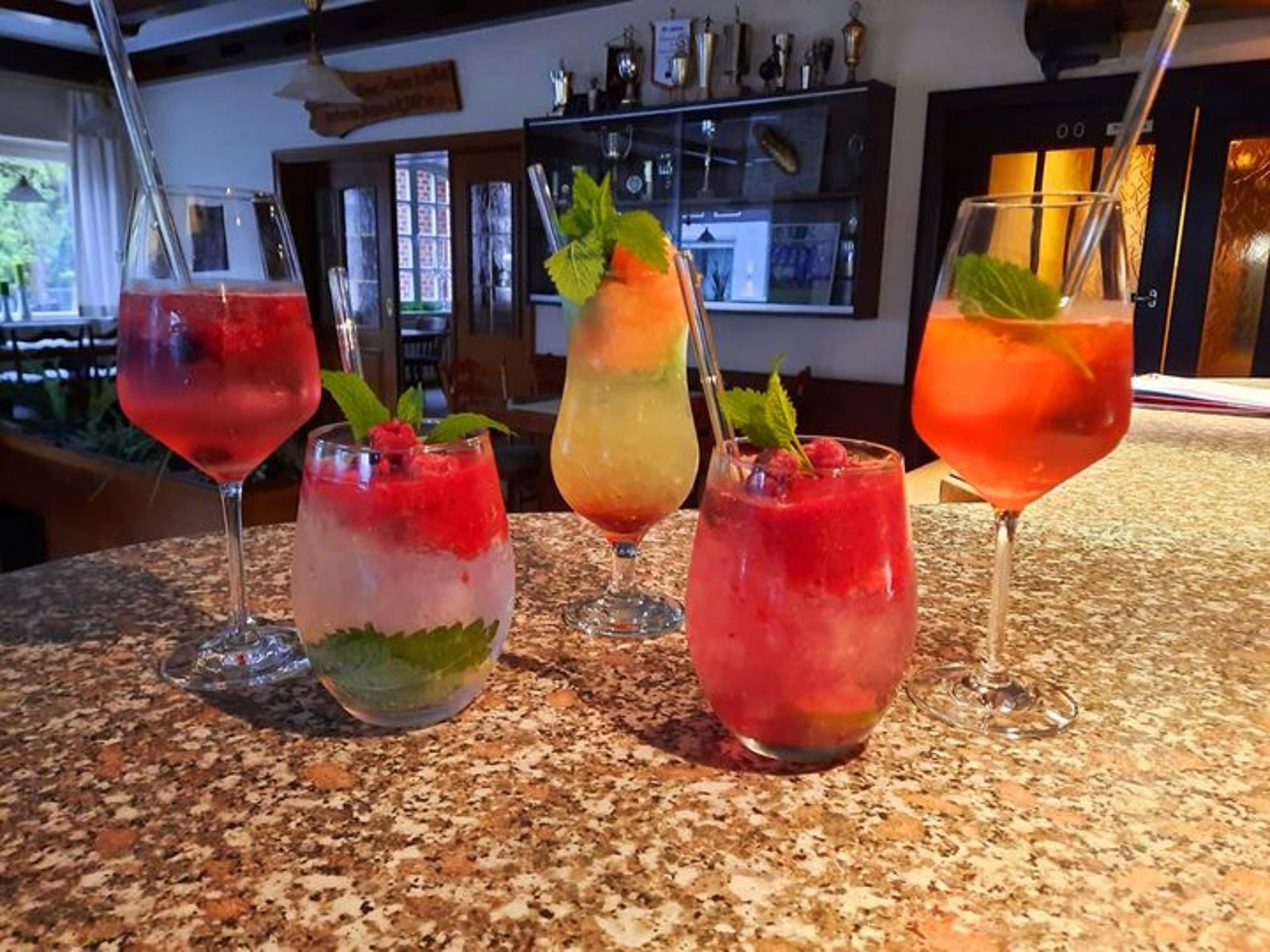Fünf bunte, hausgemachte Cocktails mit Früchten und Minze auf einem Tisch in der Gaststube